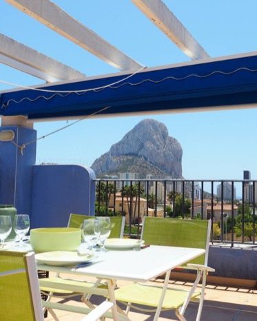 Terraza del Apartamento La Estrella con la mesa puesta bajo el toldo y el Peñón de Ifach al fondo