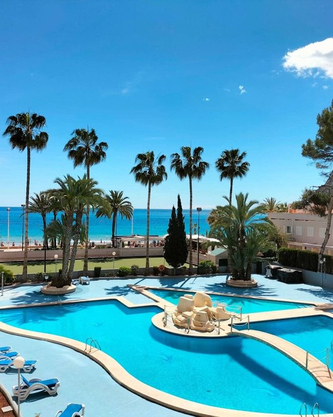 Piscina comunitaria del Apartamento Paraíso Mar entre palmeras, con el mar al fondo