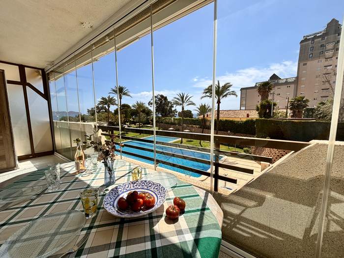 Terraza acristalada de Calpe Place con la mesa puesta y la piscina comunitaria al fondo