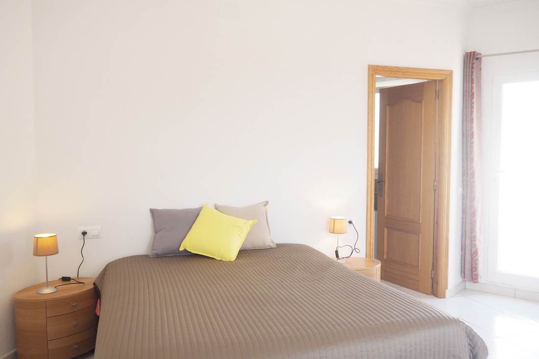 Dormitorio doble con colcha gris y cojín amarillo