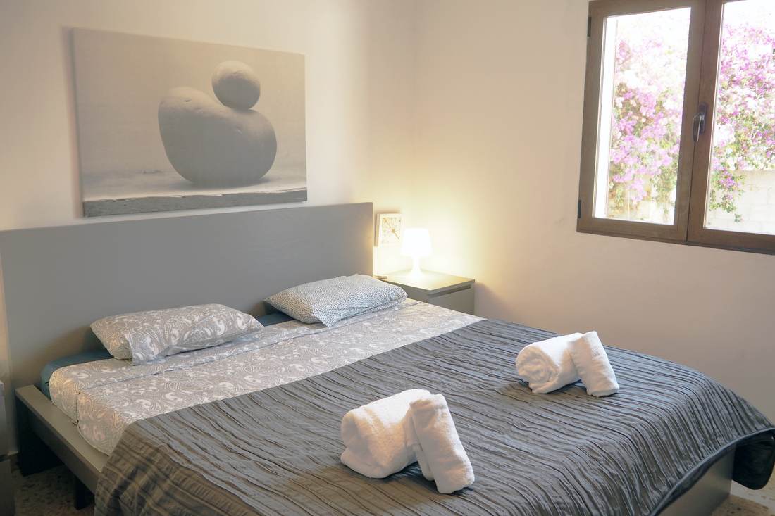 Dormitorio doble con cabecero claro y toallas dobladas
