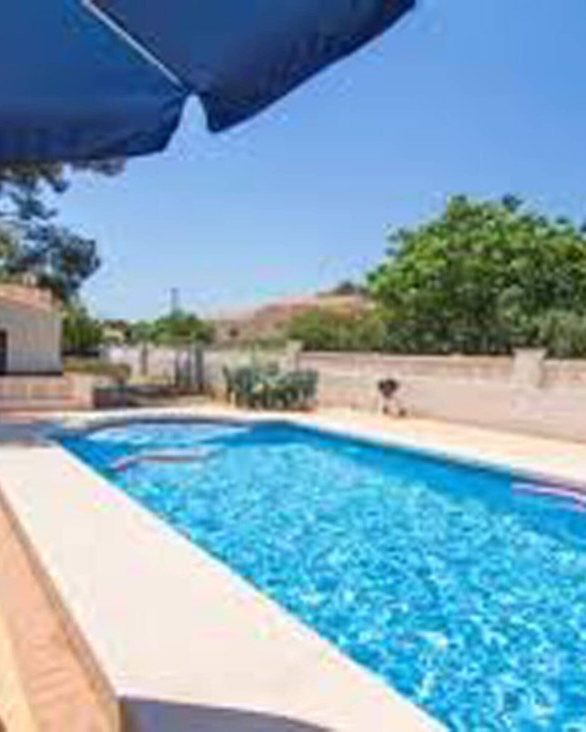 Piscina de Casa Clara con la sombrilla azul y los pinos alrededor