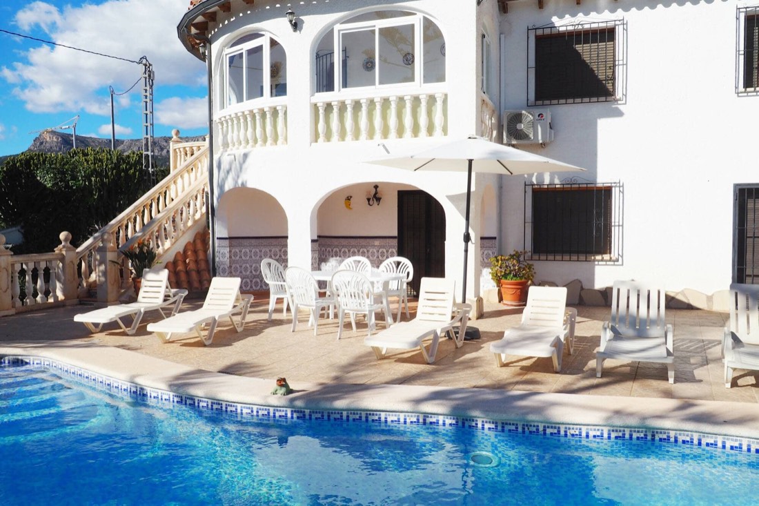 Fachada blanca de Casa Margarita con la piscina y las tumbonas en primer término
