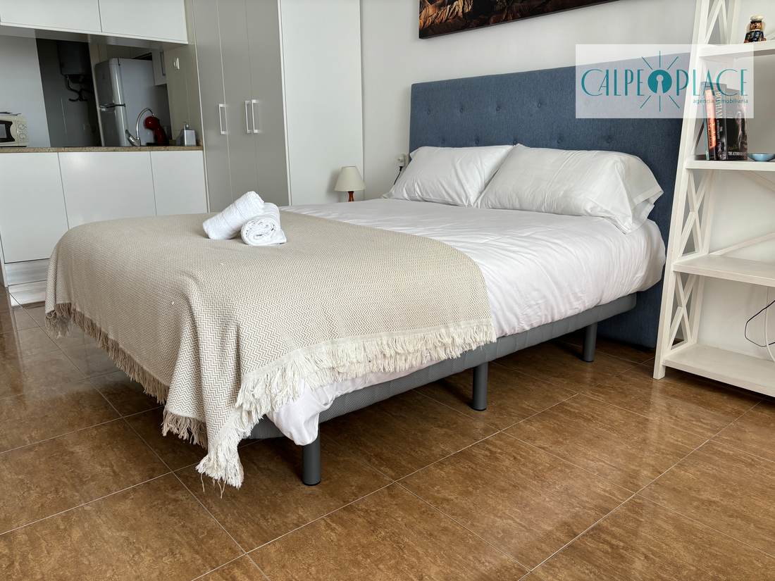 El estudio de lado a lado: la cama, la estantería blanca y la mesa junto al ventanal