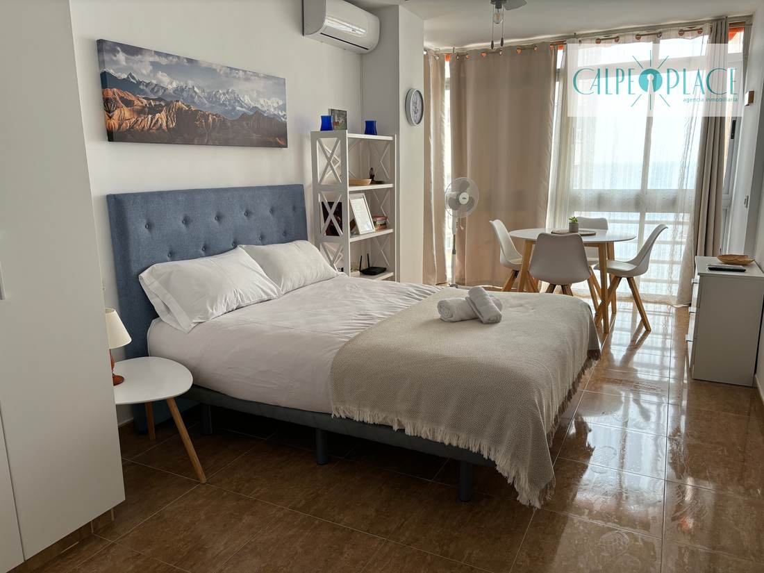 La cama con la mesita redonda al lado y la puerta de la terraza abierta