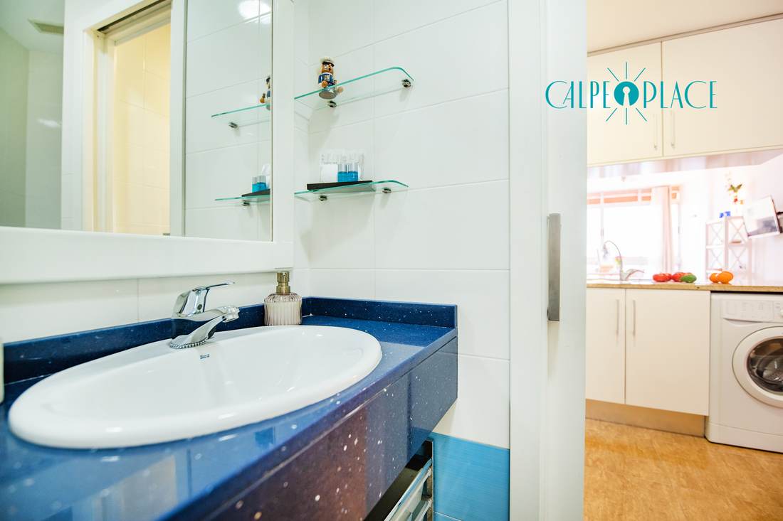 Lavabo del baño con espejo y el paso a la cocina al fondo
