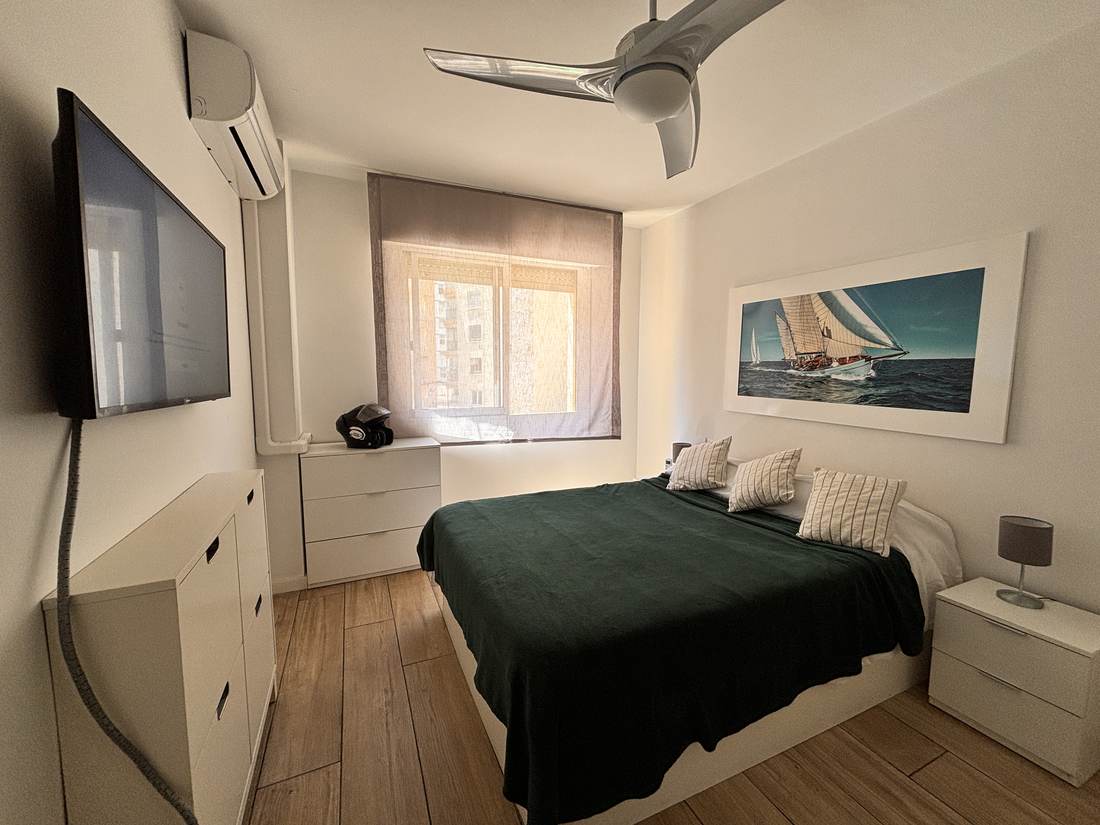 Dormitorio con colcha verde, televisión y cuadro de veleros