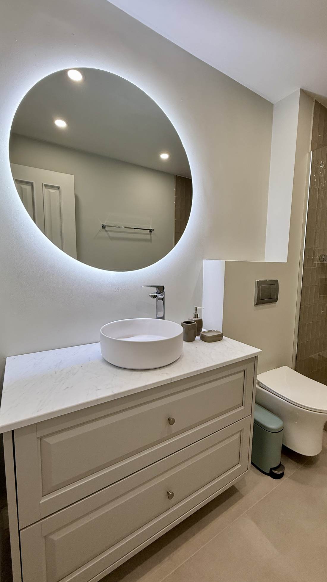 Baño con espejo redondo retroiluminado y mueble de lavabo