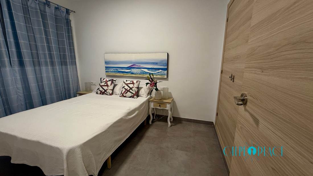 Detalle del dormitorio, con la cama hecha y el cuadro del mar