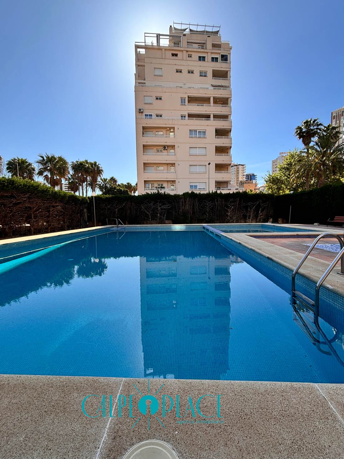Piscina comunitaria, larga y rodeada de césped