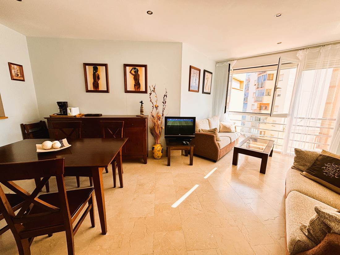 Salón y comedor de Kenya con dos sofás, mesa de madera oscura y el ventanal de la galería al fondo