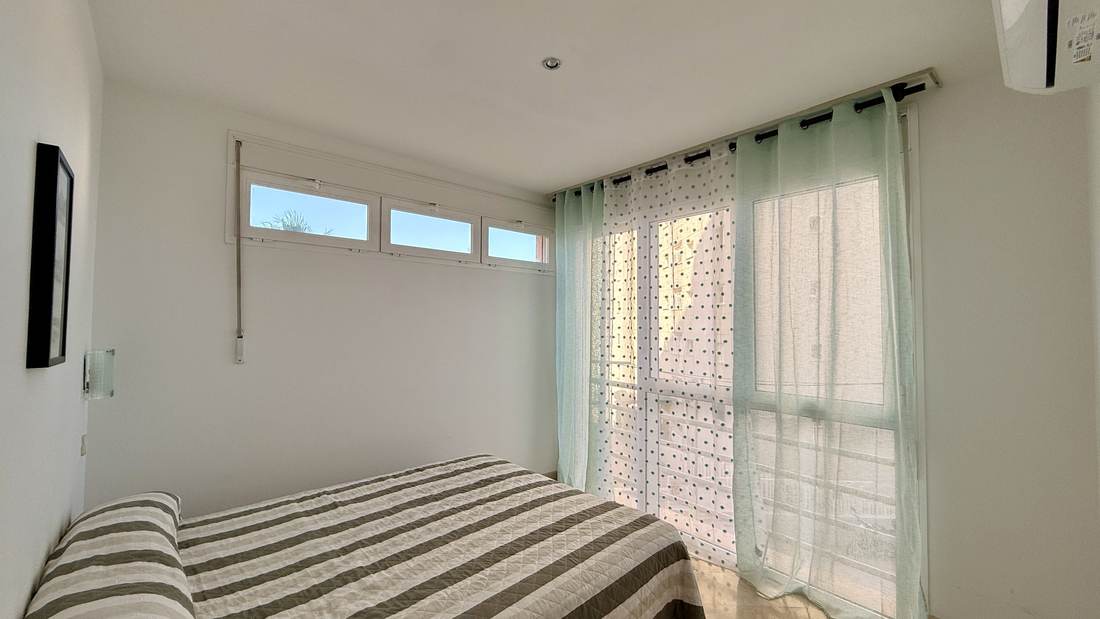 Dormitorio con colcha de rayas y aire acondicionado