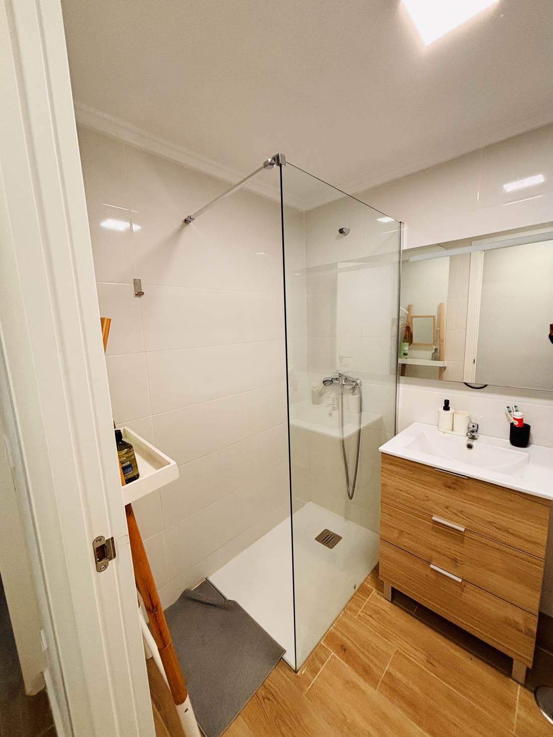 Baño con ducha de obra, mampara de cristal y mueble de madera