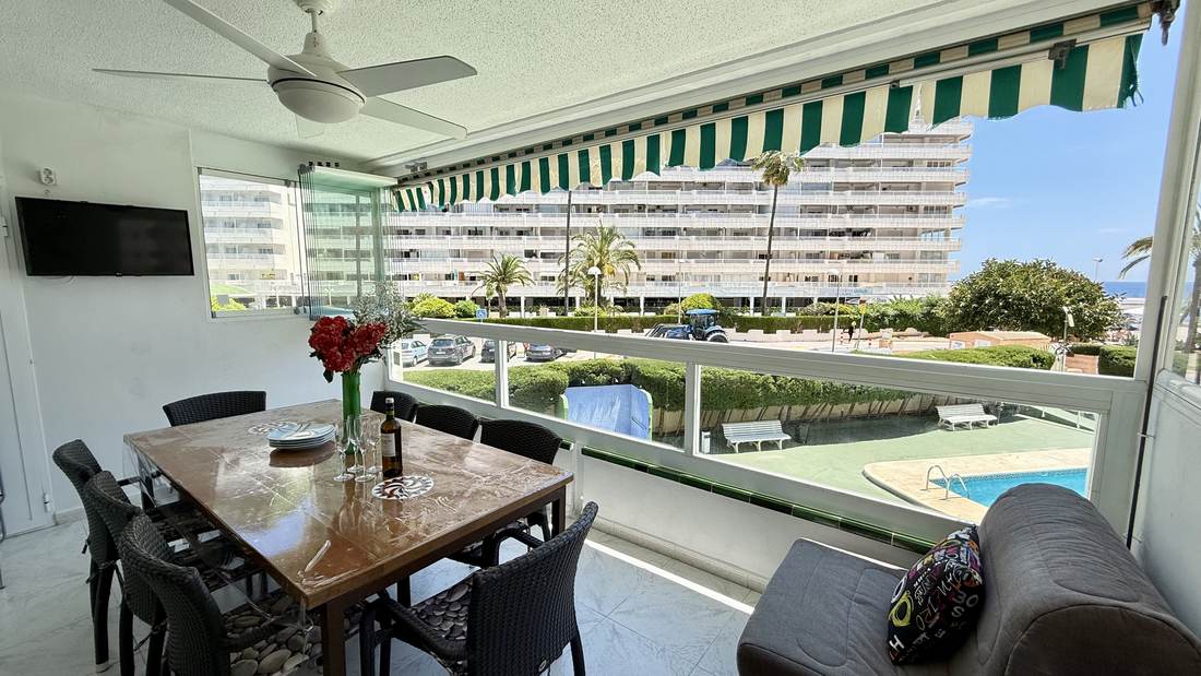 Mesa de comedor en la galería, con la piscina y la playa detrás