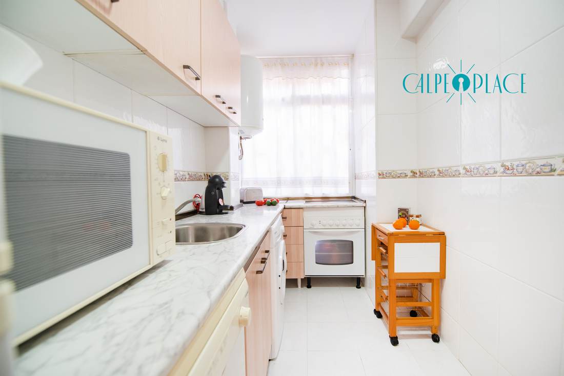 La cocina alargada de lado a lado, con la encimera y los muebles blancos