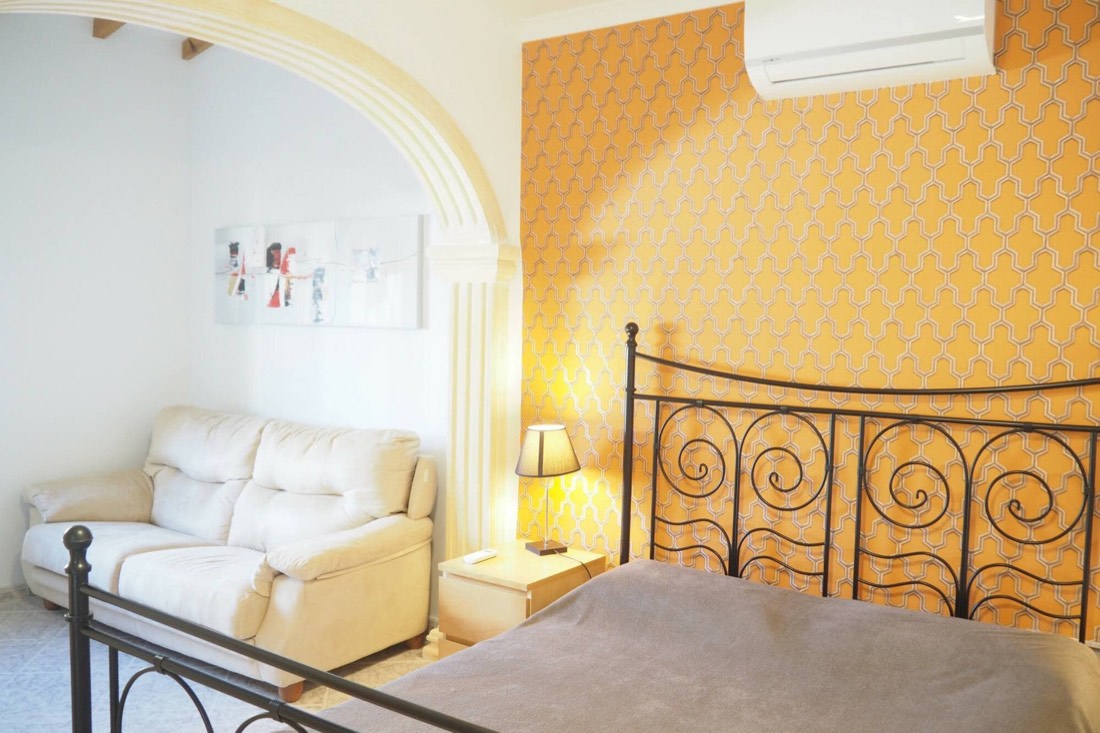 Dormitorio con cama de forja, pared amarilla y sofá