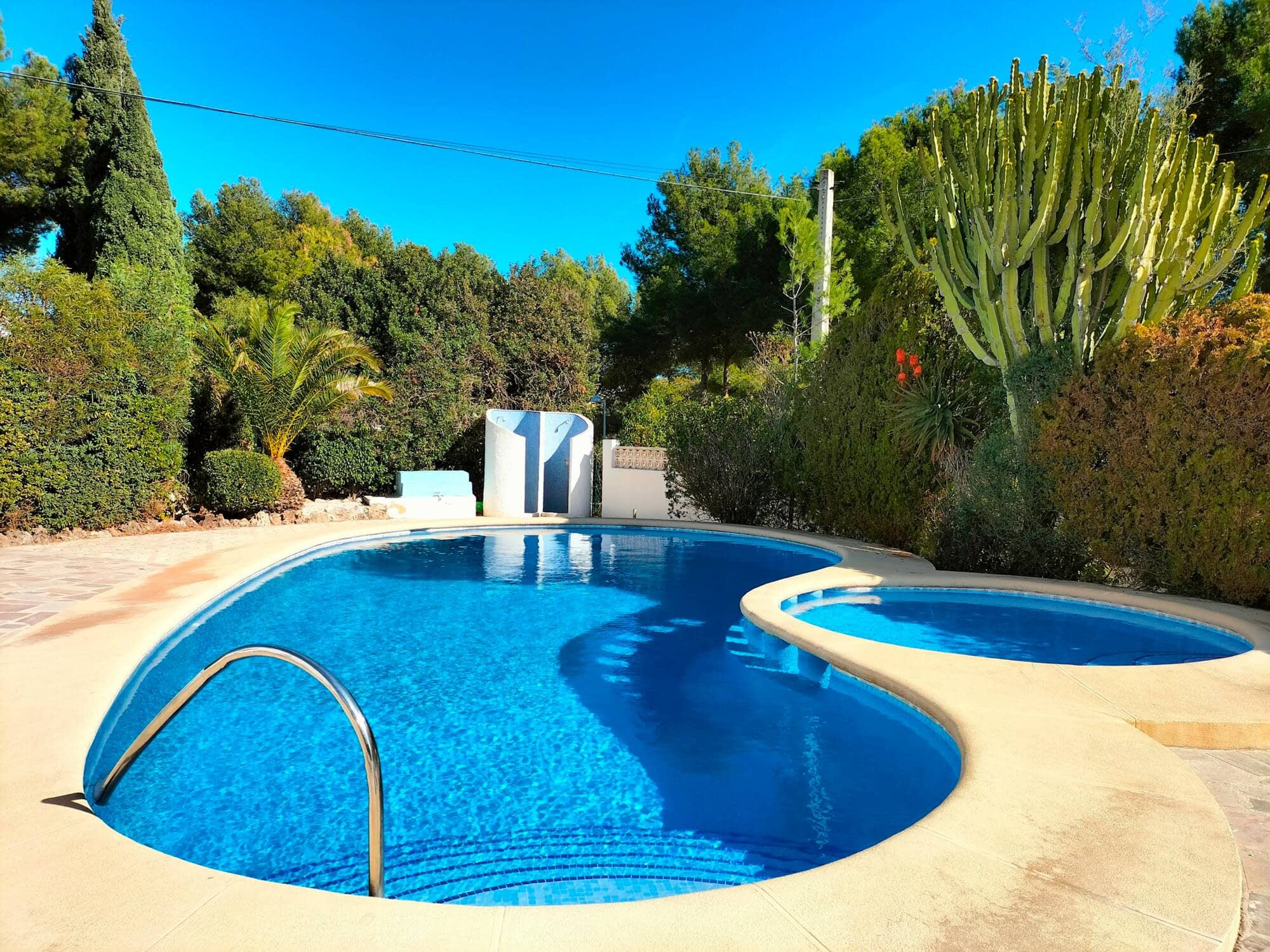 Piscina comunitaria de forma curva rodeada de vegetación mediterránea en Calpe